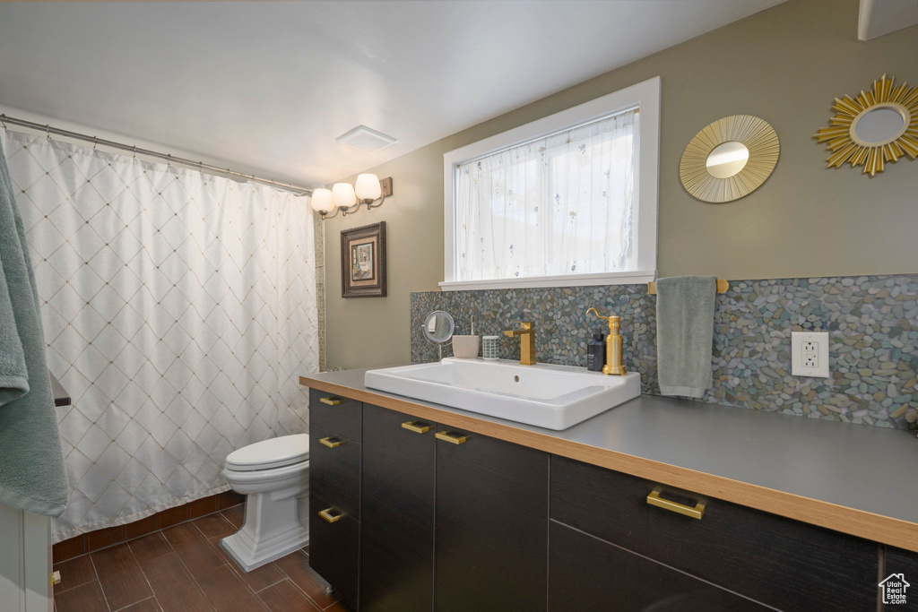 Bathroom featuring backsplash, toilet, vanity, wood finished floors, and curtained shower