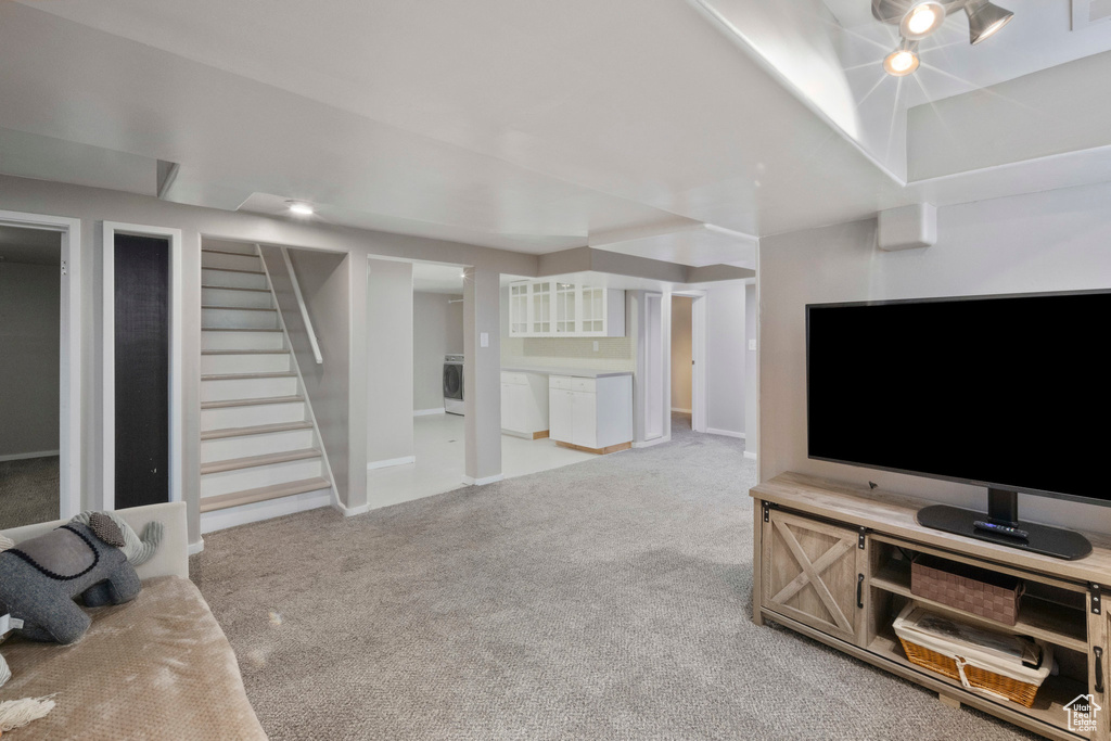 Unfurnished living room with washer / dryer, light colored carpet, and stairs