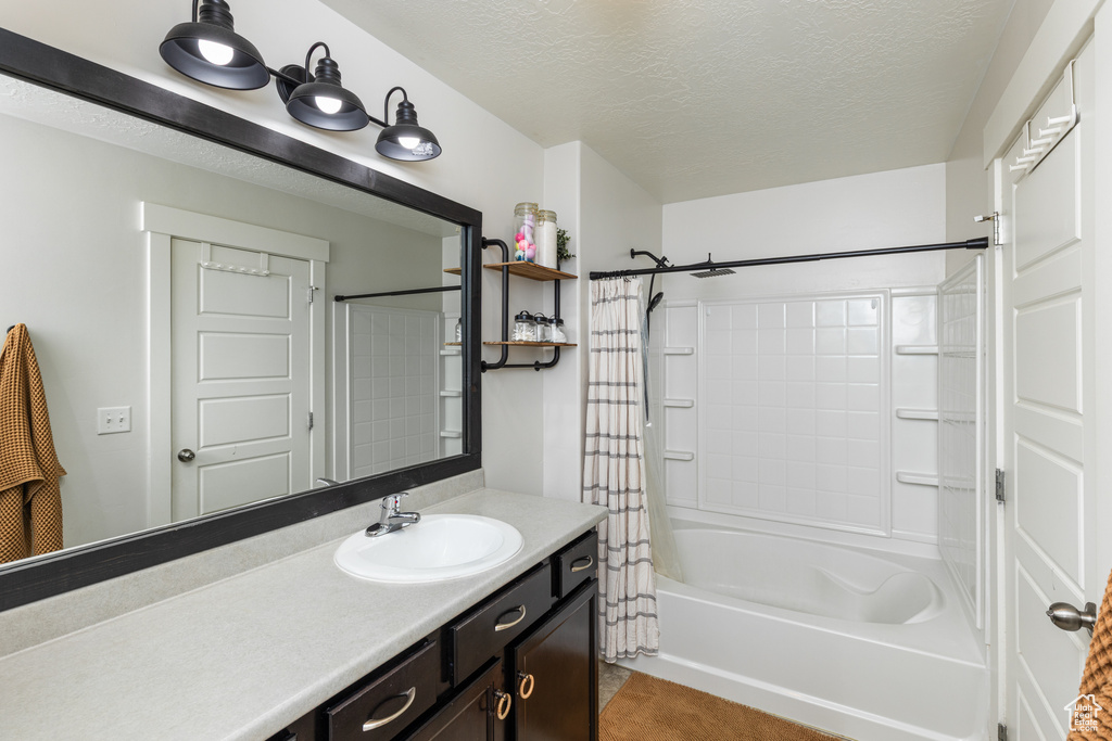 Full bathroom with vanity, shower / bathtub combination with curtain, and a textured ceiling