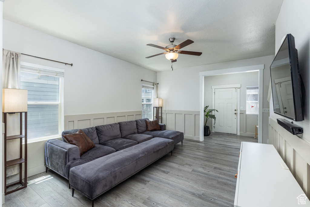 Living room with ceiling fan, light wood-type flooring, and wainscoting