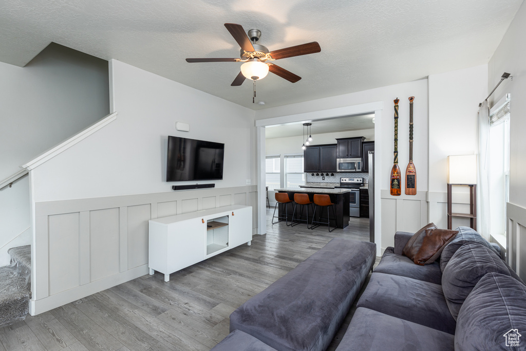 Living area with ceiling fan, light wood finished floors, a wainscoted wall, and stairway