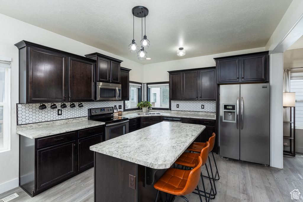 Kitchen with stainless steel appliances, light wood-style flooring, a sink, and tasteful backsplash
