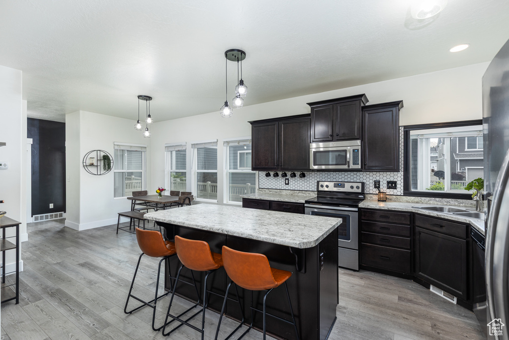 Kitchen with stainless steel appliances, a center island, light wood-style floors, and tasteful backsplash