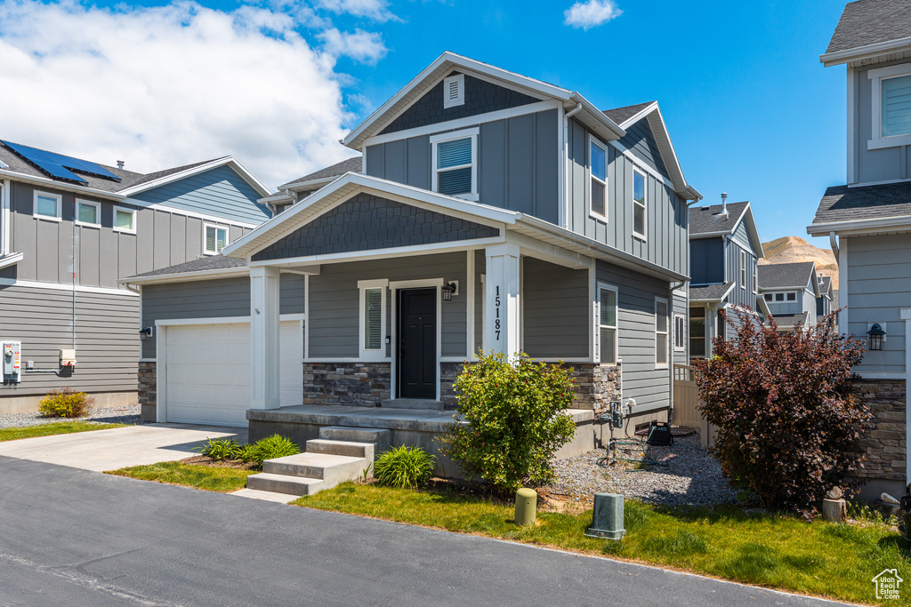 View of front of home featuring board and batten siding, driveway, a porch, a garage, and stone siding