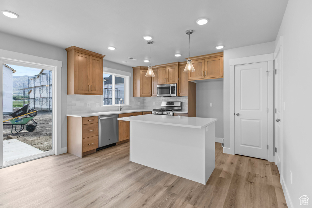 Kitchen with appliances with stainless steel finishes, light wood-style floors, brown cabinets, light countertops, and decorative light fixtures