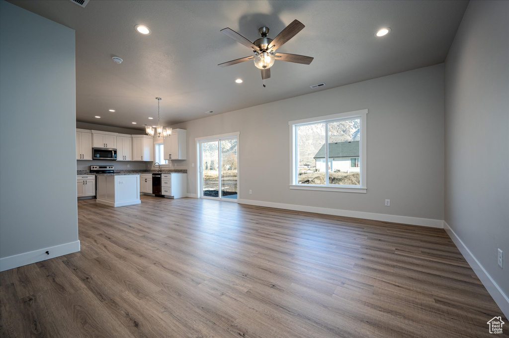 Unfurnished living room with recessed lighting, a chandelier, baseboards, wood finished floors, and a ceiling fan