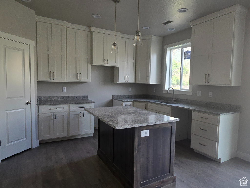 Kitchen with wood finished floors, a kitchen island, white cabinetry, light stone counters, and recessed lighting