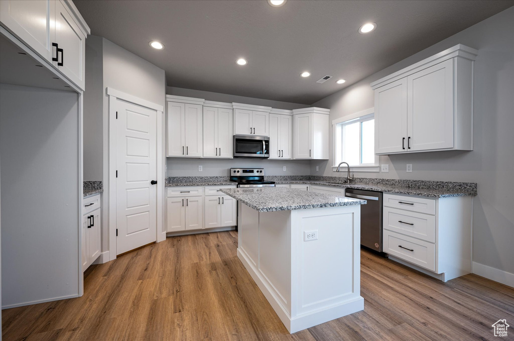 Kitchen with appliances with stainless steel finishes, light wood finished floors, white cabinets, recessed lighting, and a center island