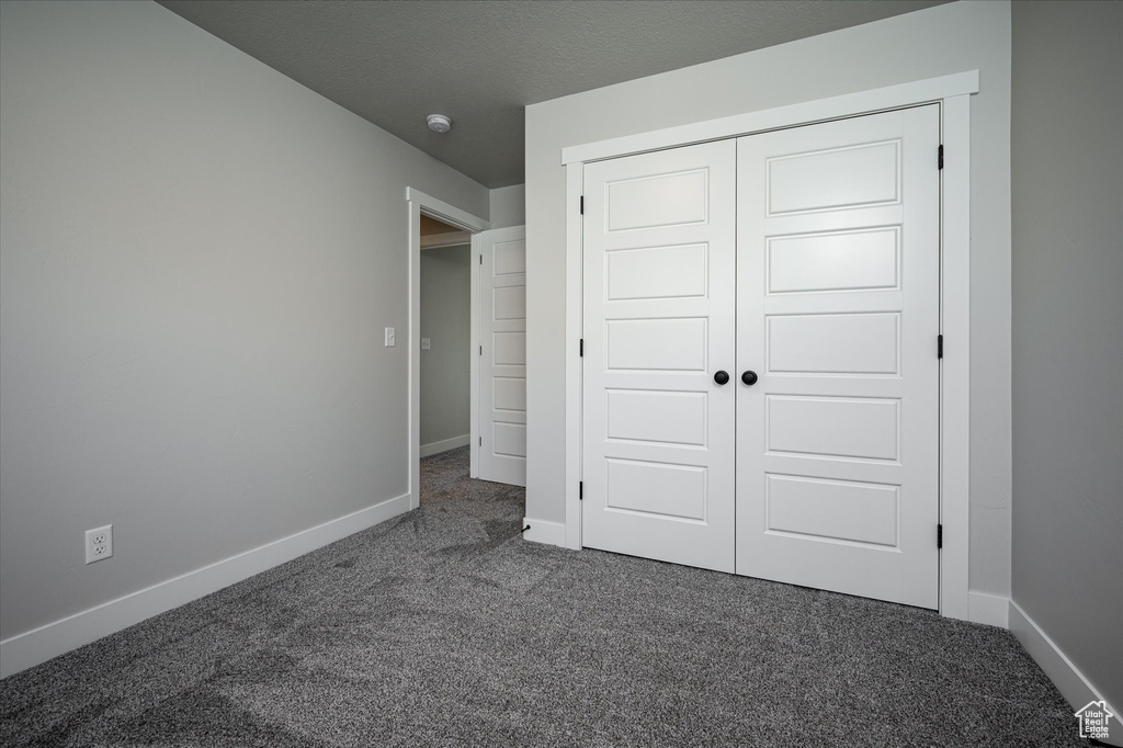 Unfurnished bedroom featuring dark carpet, baseboards, and a closet