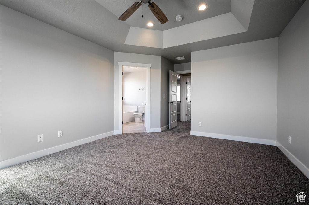 Unfurnished bedroom with a tray ceiling, carpet floors, recessed lighting, baseboards, and ensuite bath
