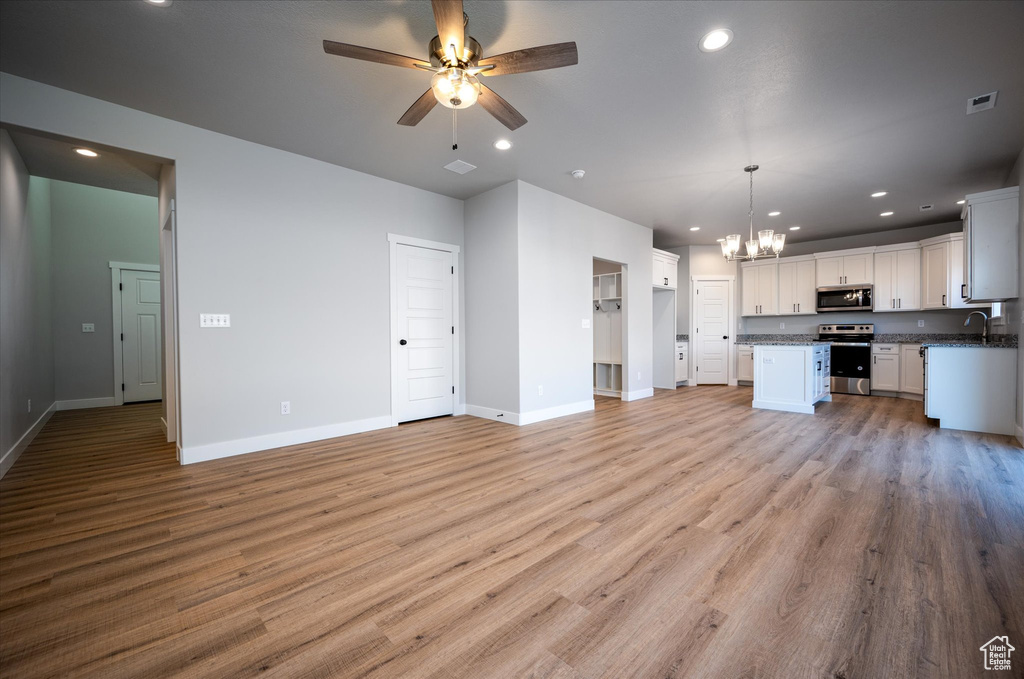 Unfurnished living room with a chandelier, a ceiling fan, recessed lighting, baseboards, and light wood-type flooring