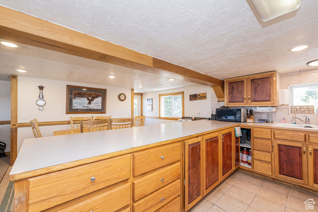 Kitchen with black microwave, a peninsula, a sink, recessed lighting, and light countertops