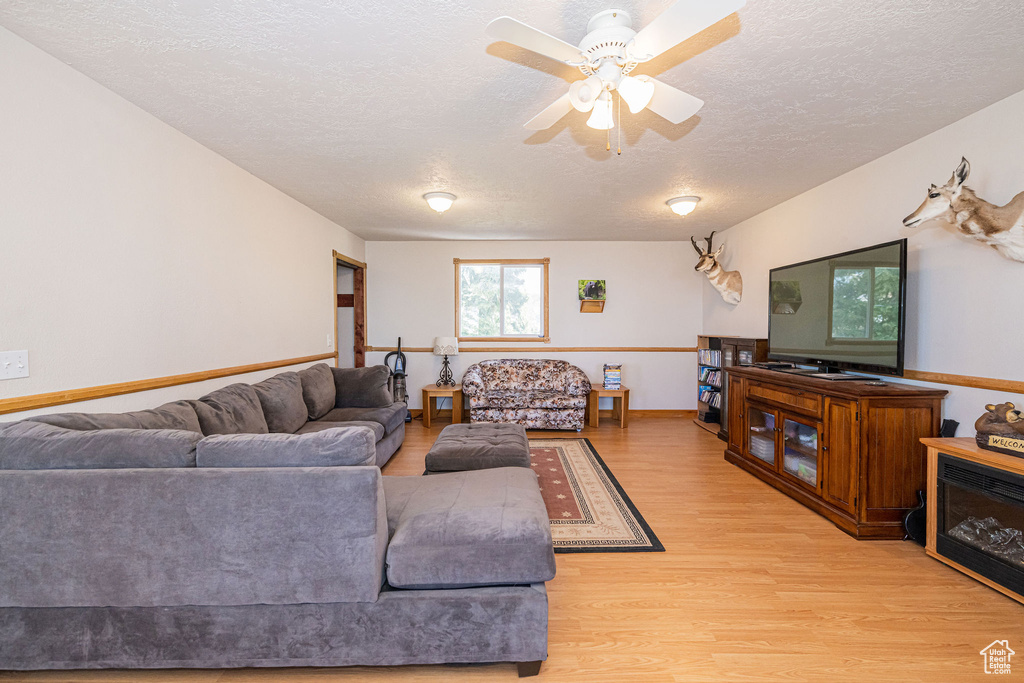 Living area featuring a textured ceiling, light wood finished floors, a ceiling fan, and baseboards