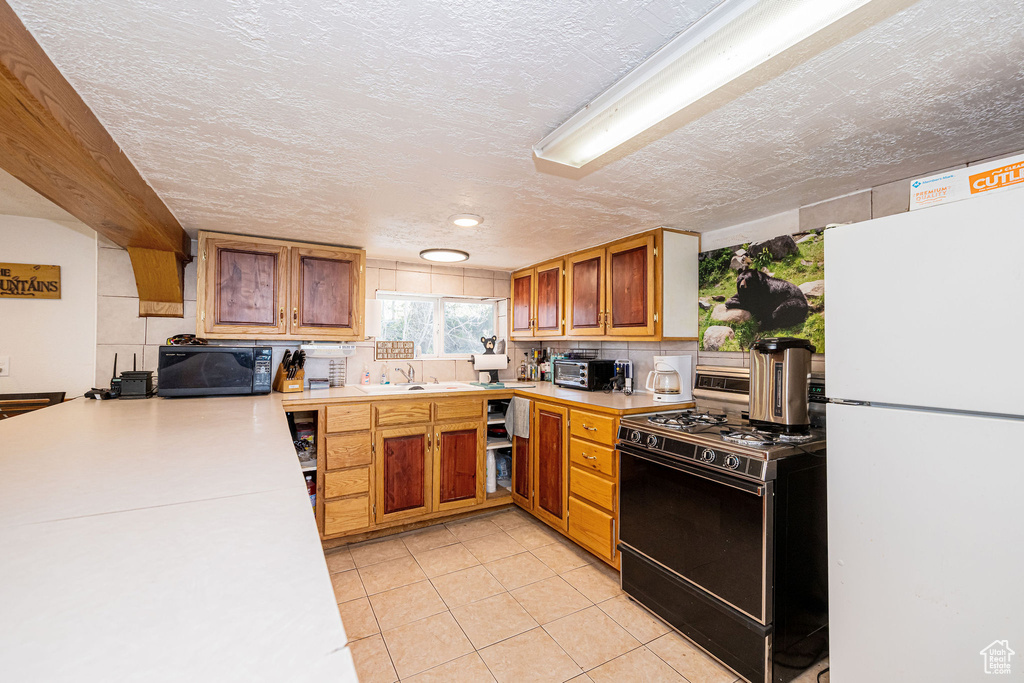 Kitchen featuring freestanding refrigerator, gas range, black microwave, light countertops, and a textured ceiling