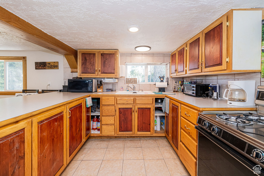 Kitchen featuring black appliances, a sink, light countertops, tasteful backsplash, and a textured ceiling
