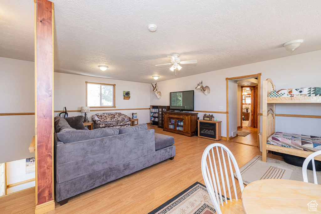 Living area with light wood-style floors, a ceiling fan, a textured ceiling, and baseboards