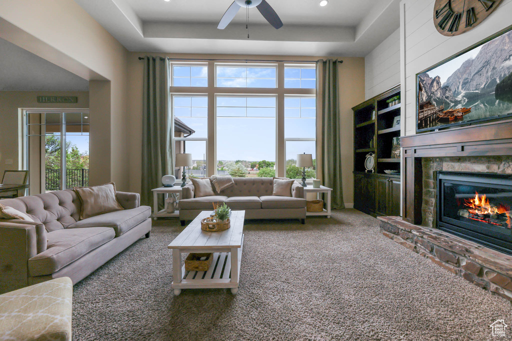 Living room featuring a ceiling fan, carpet floors, a raised ceiling, and a high end fireplace