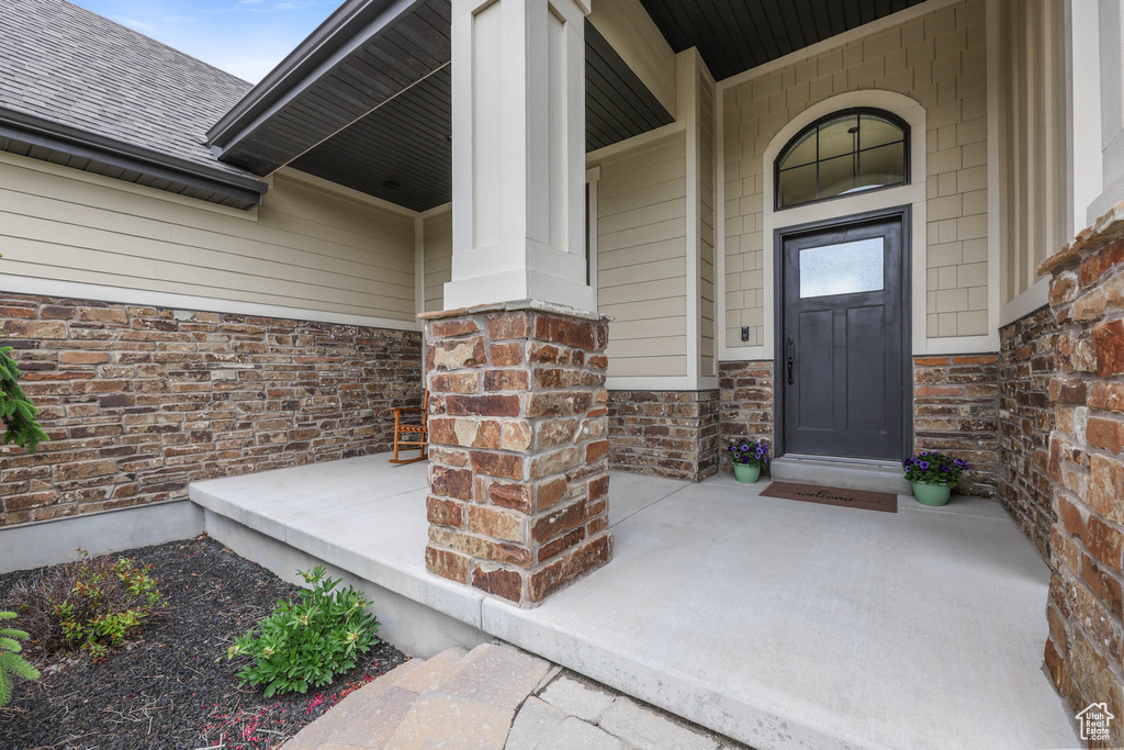 Property entrance with a porch, a shingled roof, and stone siding