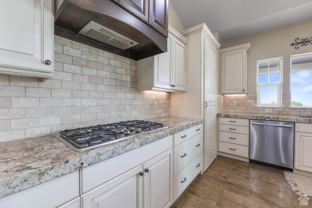 Kitchen featuring stainless steel appliances, under cabinet range hood, dark wood-style flooring, decorative backsplash, and white cabinetry