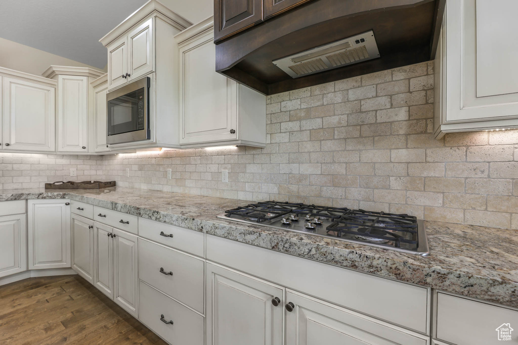 Kitchen featuring range hood, appliances with stainless steel finishes, tasteful backsplash, light stone counters, and dark wood-style flooring