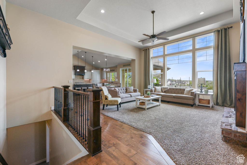 Living room with wood-type flooring, a ceiling fan, recessed lighting, and a raised ceiling