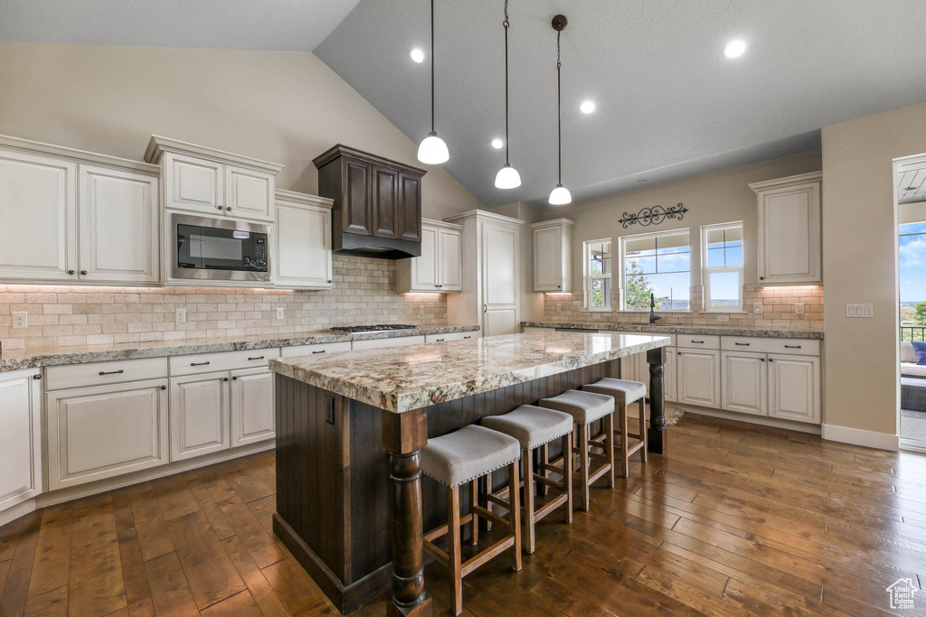 Kitchen with stainless steel microwave, a center island, dark wood-style flooring, a kitchen breakfast bar, and tasteful backsplash