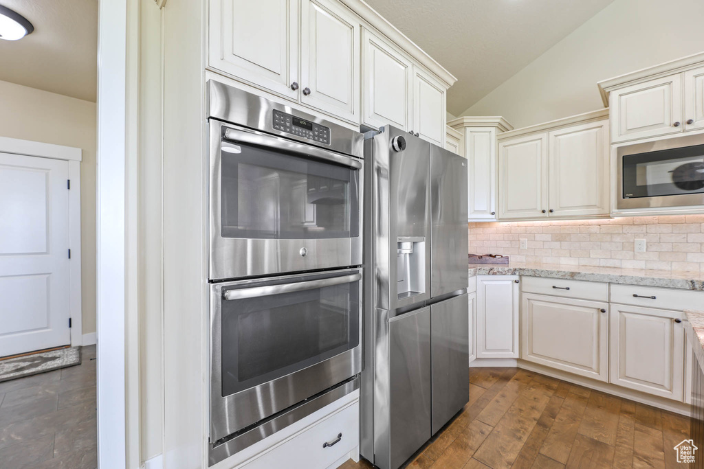 Kitchen with stainless steel appliances, lofted ceiling, backsplash, light stone countertops, and dark wood finished floors