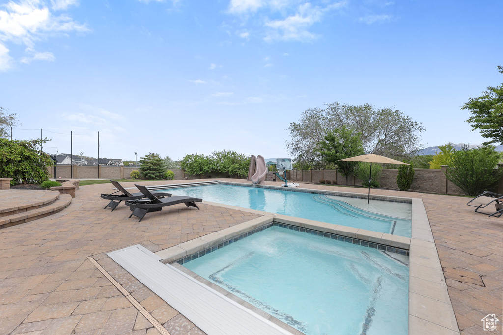 View of pool featuring a water slide, an in-ground hot tub, a fenced backyard, and a patio area