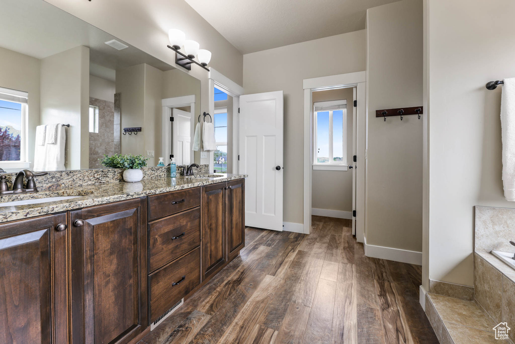 Full bathroom featuring wood finished floors, double vanity, tiled bath, baseboards, and a tile shower