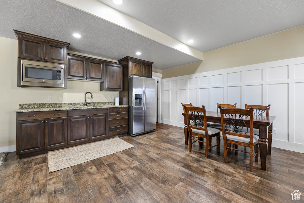 Kitchen featuring appliances with stainless steel finishes, a decorative wall, dark brown cabinetry, dark wood finished floors, and a sink