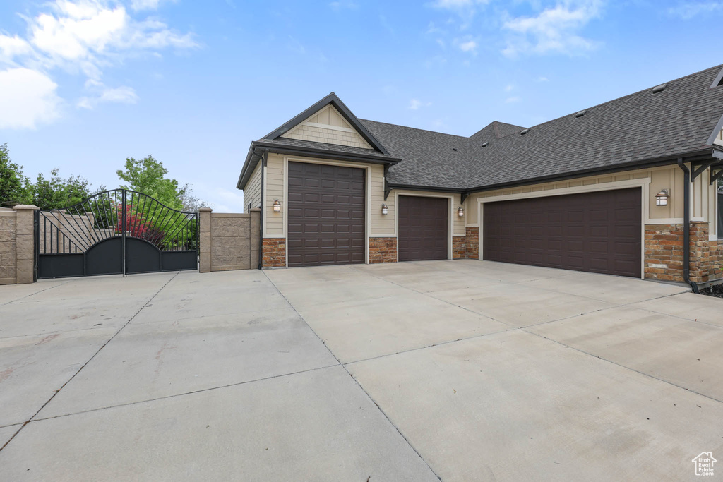 View of front facade featuring a gate, driveway, an attached garage, stone siding, and a shingled roof