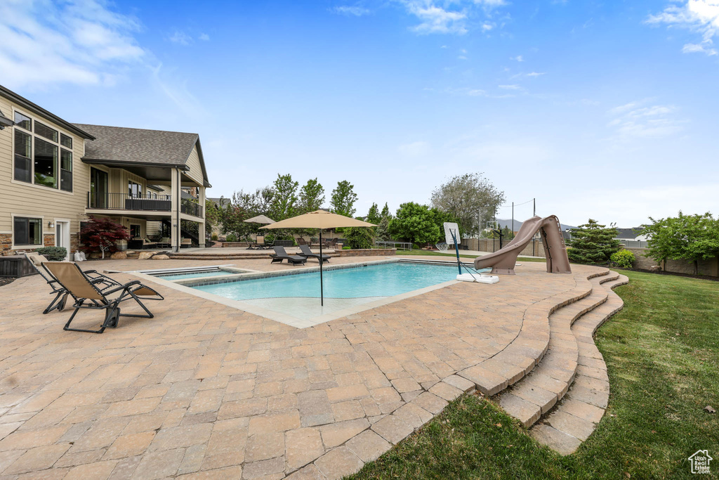 View of swimming pool with a water slide, a patio area, and a pool with connected hot tub