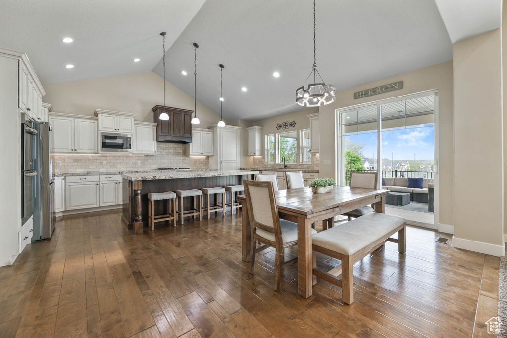 Dining area with dark wood-style floors, high vaulted ceiling, a chandelier, and recessed lighting