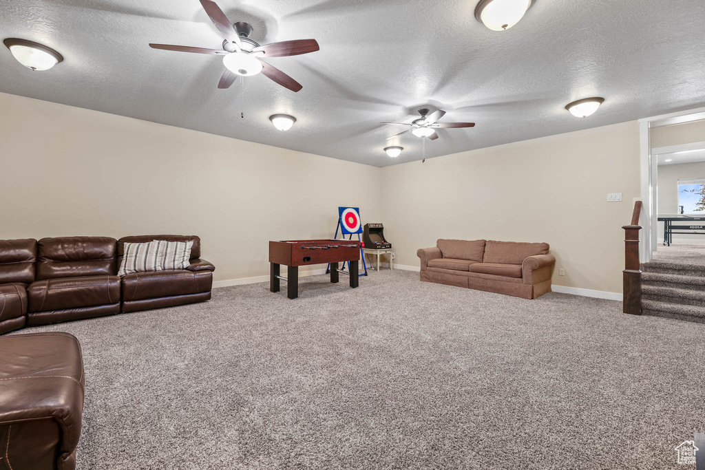 Carpeted living room featuring a ceiling fan, a textured ceiling, baseboards, and stairway