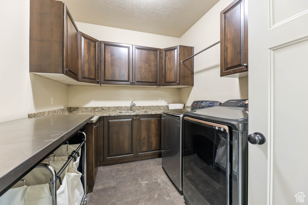 Laundry room with cabinet space, washing machine and dryer, a textured ceiling, and stone finish floors