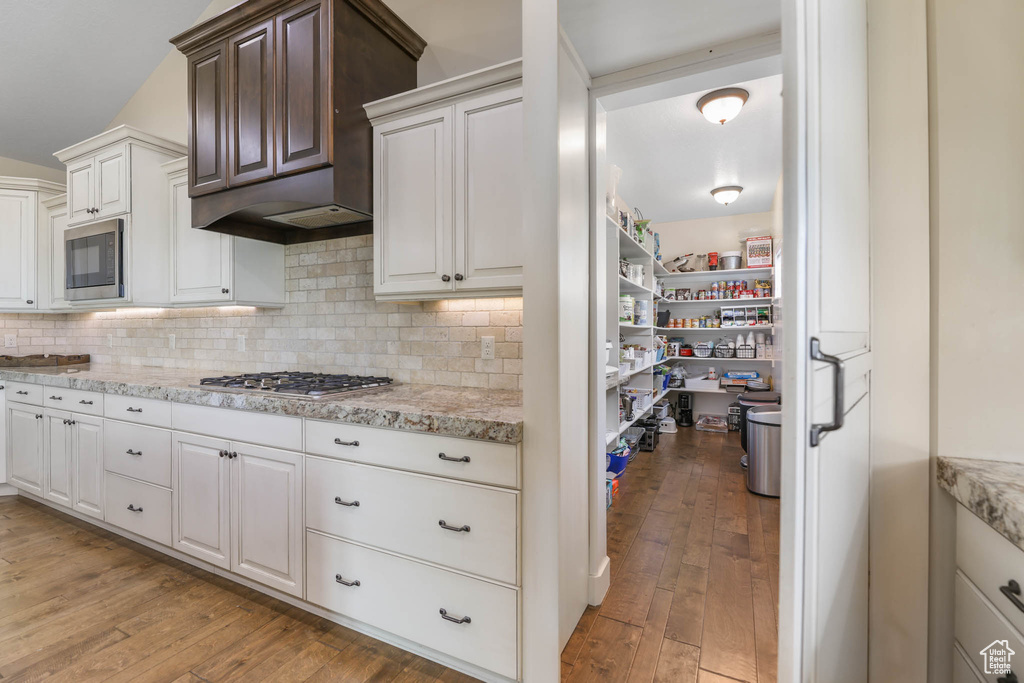 Kitchen with appliances with stainless steel finishes, light wood finished floors, tasteful backsplash, and white cabinetry