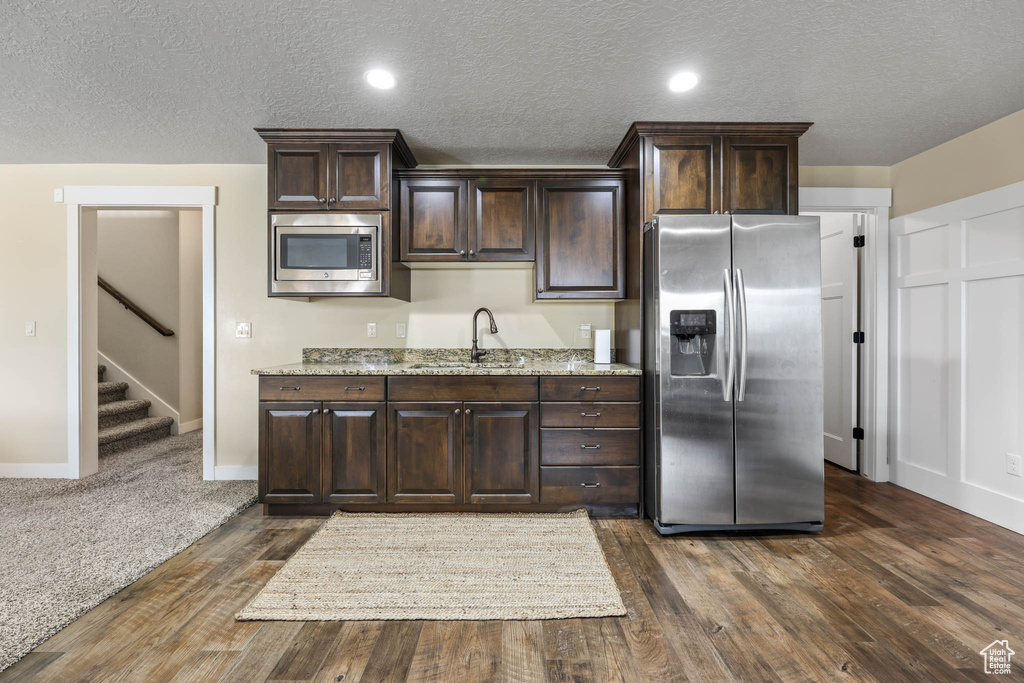 Kitchen featuring stainless steel appliances, a sink, dark brown cabinetry, dark wood-style flooring, and a textured ceiling