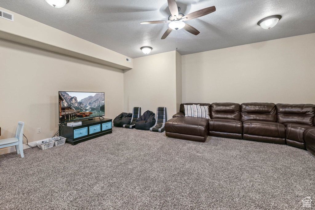 Carpeted home theater room featuring ceiling fan and a textured ceiling