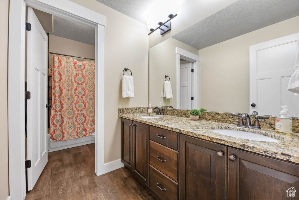 Full bathroom featuring wood finished floors, double vanity, baseboards, and a textured ceiling