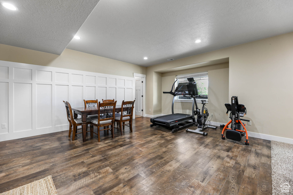 Exercise area featuring dark wood-style flooring, recessed lighting, a textured ceiling, a decorative wall, and baseboards
