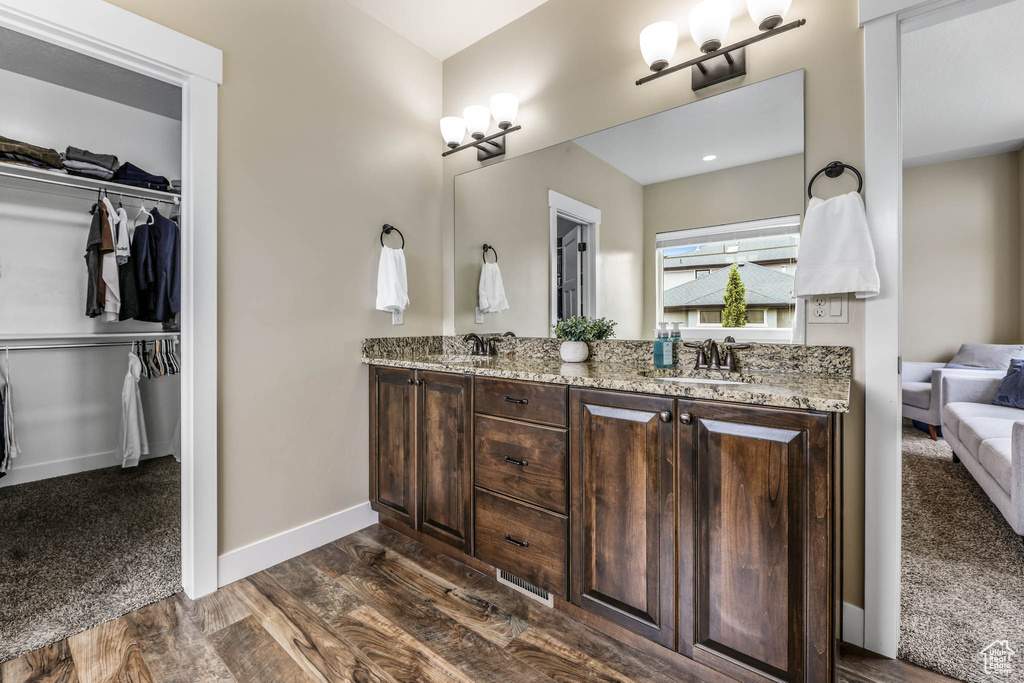 Bathroom featuring wood finished floors, double vanity, a spacious closet, and baseboards