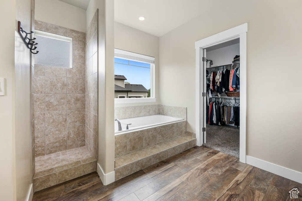 Bathroom with wood finished floors, a bath, a tile shower, a spacious closet, and baseboards