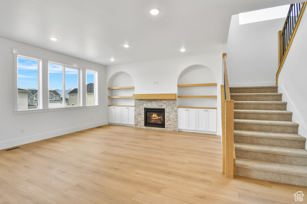 Unfurnished living room featuring stairs, baseboards, light wood-type flooring, recessed lighting, and a glass covered fireplace