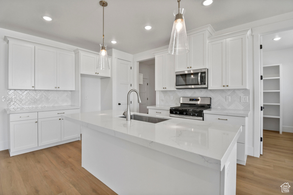 Kitchen featuring stainless steel appliances, a sink, white cabinetry, a kitchen island with sink, and decorative backsplash