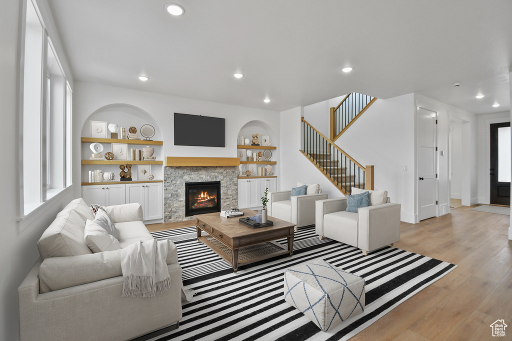 Living area with light wood-style floors, a stone fireplace, baseboards, recessed lighting, and stairs