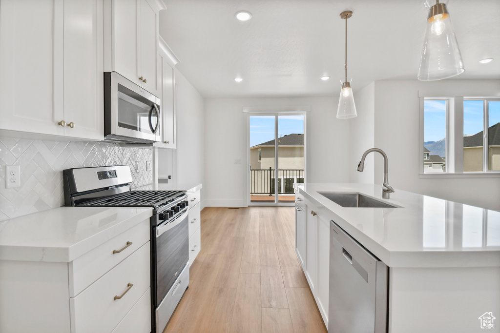 Kitchen with appliances with stainless steel finishes, a sink, backsplash, an island with sink, and light countertops
