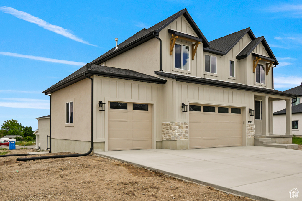 View of front facade with board and batten siding, an attached garage, driveway, stone siding, and a shingled roof