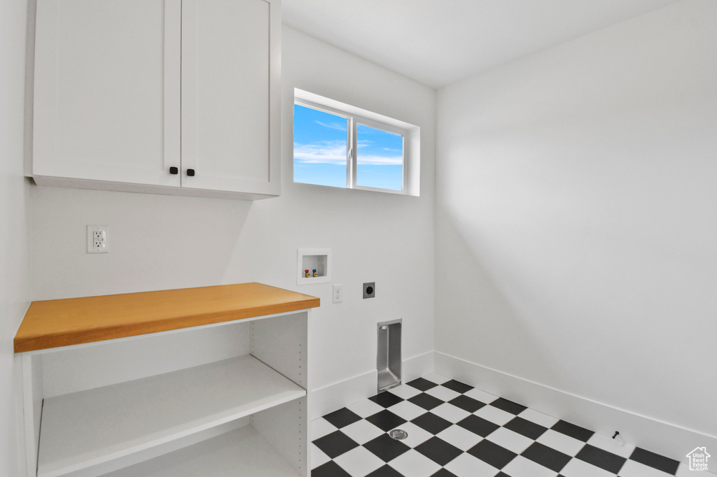 Laundry area with tile patterned floors, hookup for a washing machine, electric dryer hookup, cabinet space, and baseboards