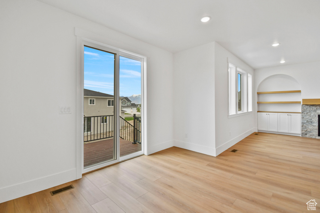 Unfurnished living room featuring baseboards, light wood-style floors, recessed lighting, a fireplace, and built in shelves