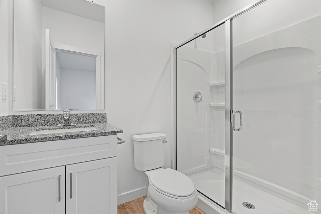 Bathroom featuring a stall shower, toilet, vanity, wood finished floors, and baseboards